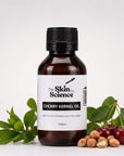 A 100ml bottle of Cherry Kernel Oil by The Skin Co. Science, in an amber glass bottle with a black cap and a white label, styled with fresh cherry leaves, cherries, and whole nuts on a white background.