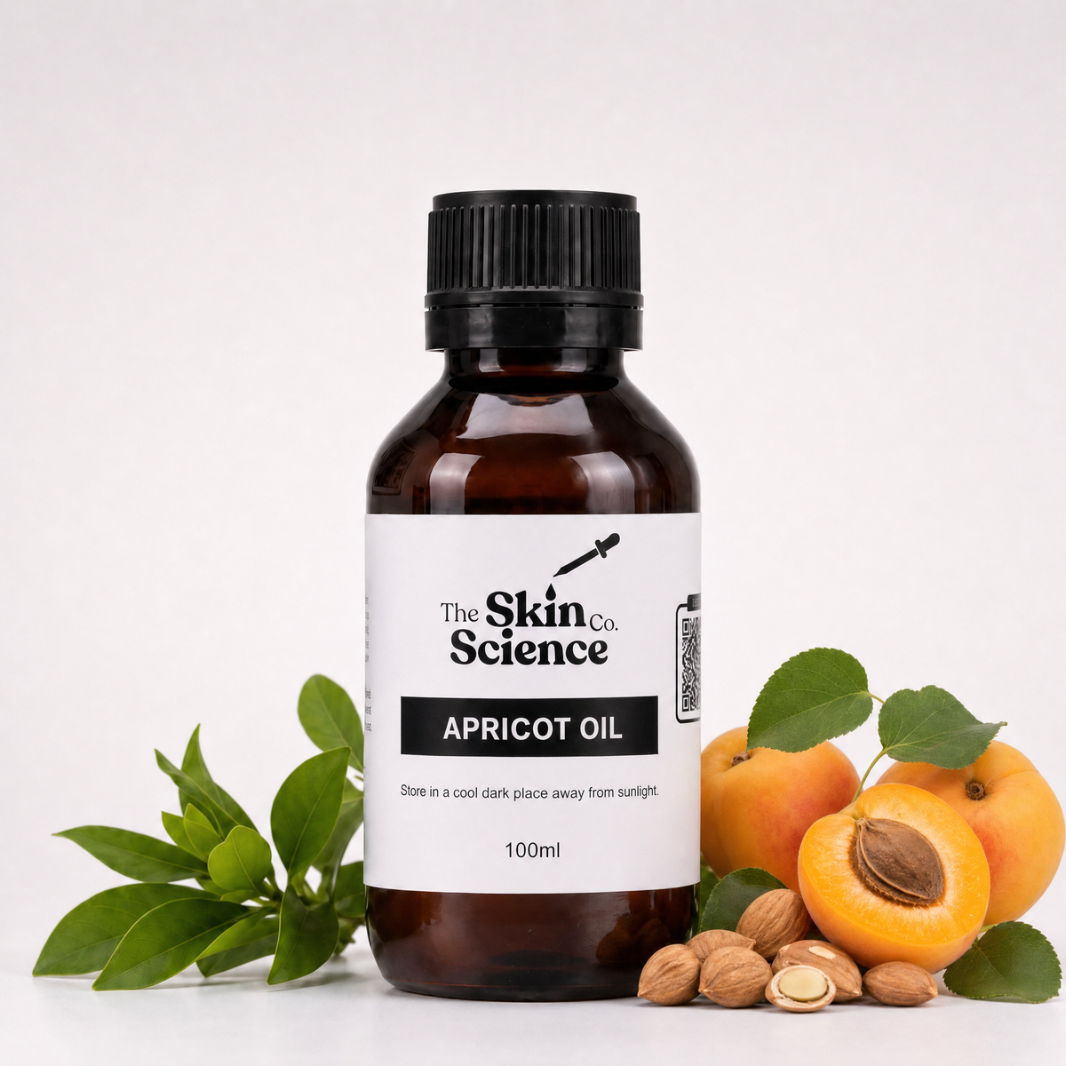 A 100ml bottle of Apricot Oil by The Skin Co. Science, presented in an amber glass bottle with a black cap and a white label, styled with fresh apricots, a halved apricot, green leaves, and almonds on a clean white background.